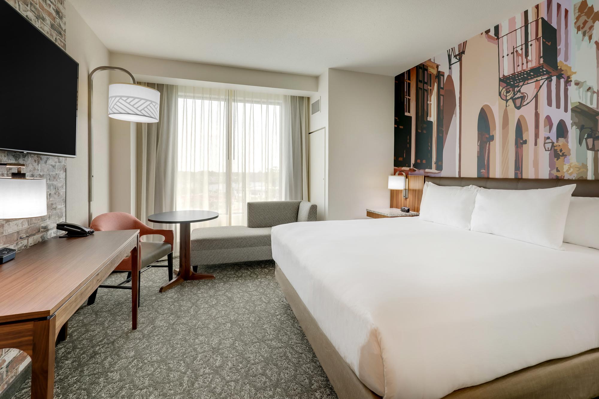 King guest room at Drury Plaza Hotel Tampa Brandon with a New Orleans-style architectural mural above the headboard, work desk, and floor-to-ceiling window.