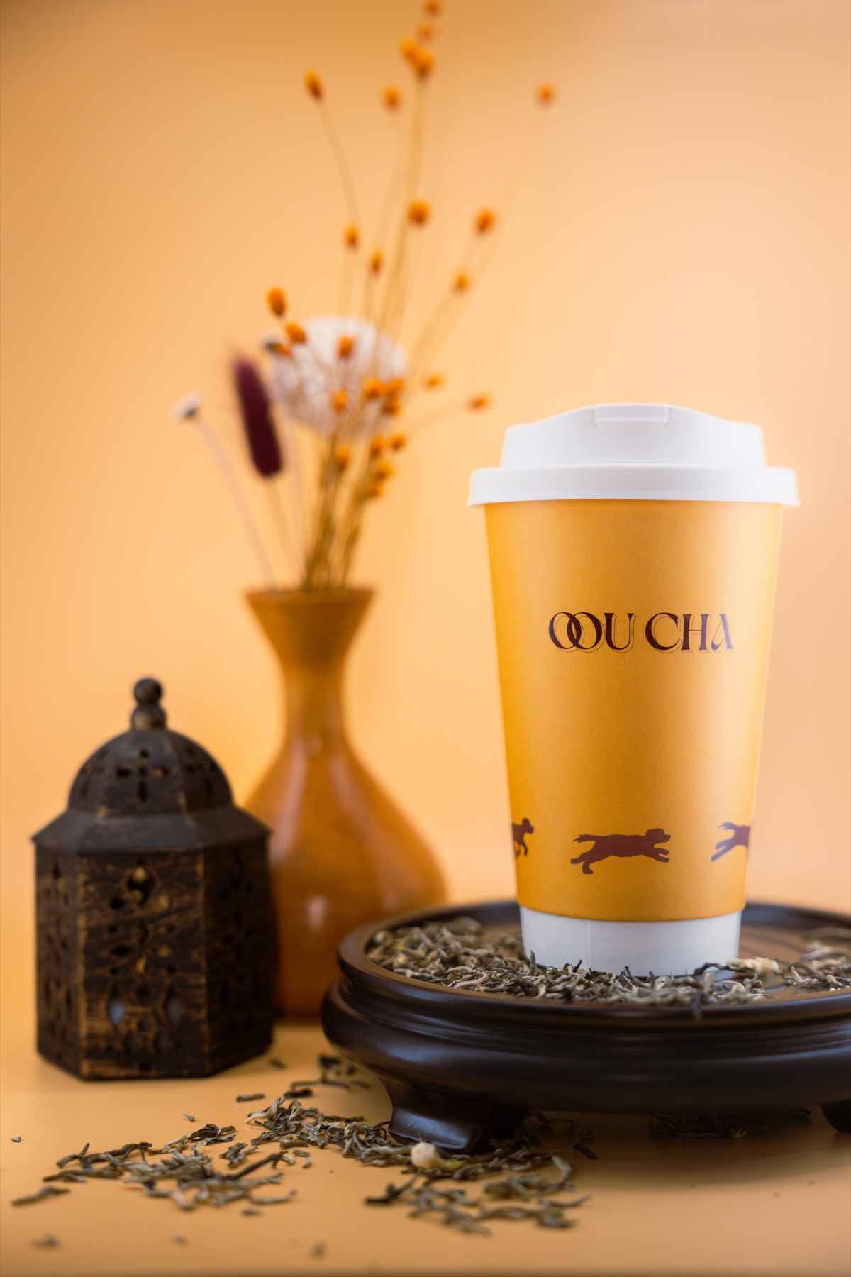 Loose-leaf tea spilling around a branded Oou Cha cup beside a carved lantern