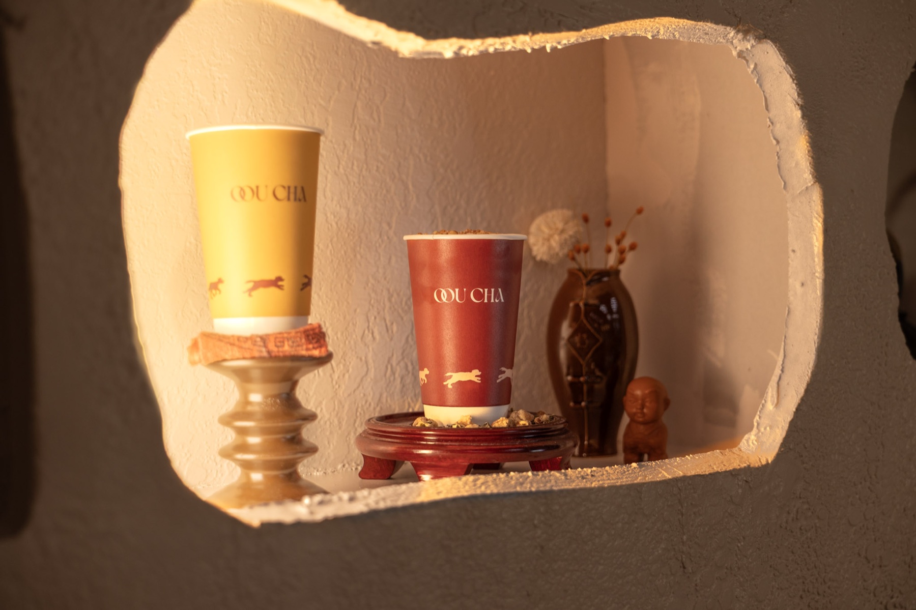 Yellow and red Oou Cha cups displayed in an arched wall niche beside a vase and small figurine