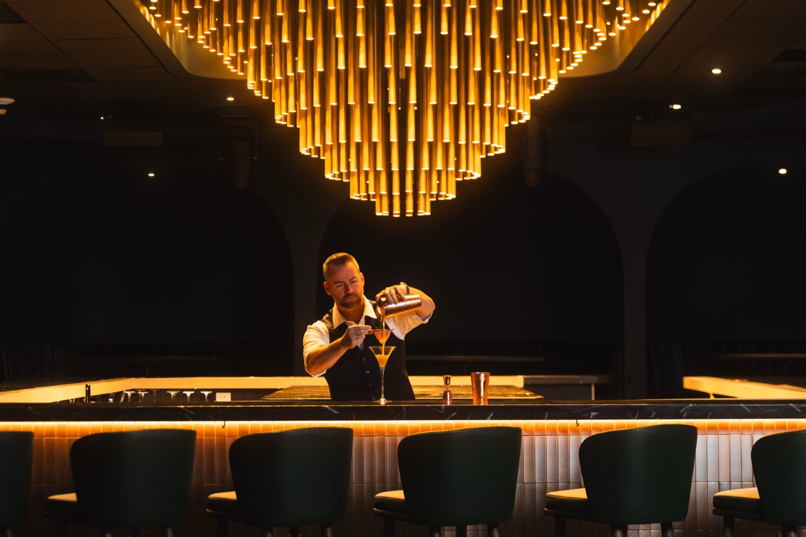 Bartender straining a cocktail beneath warm light