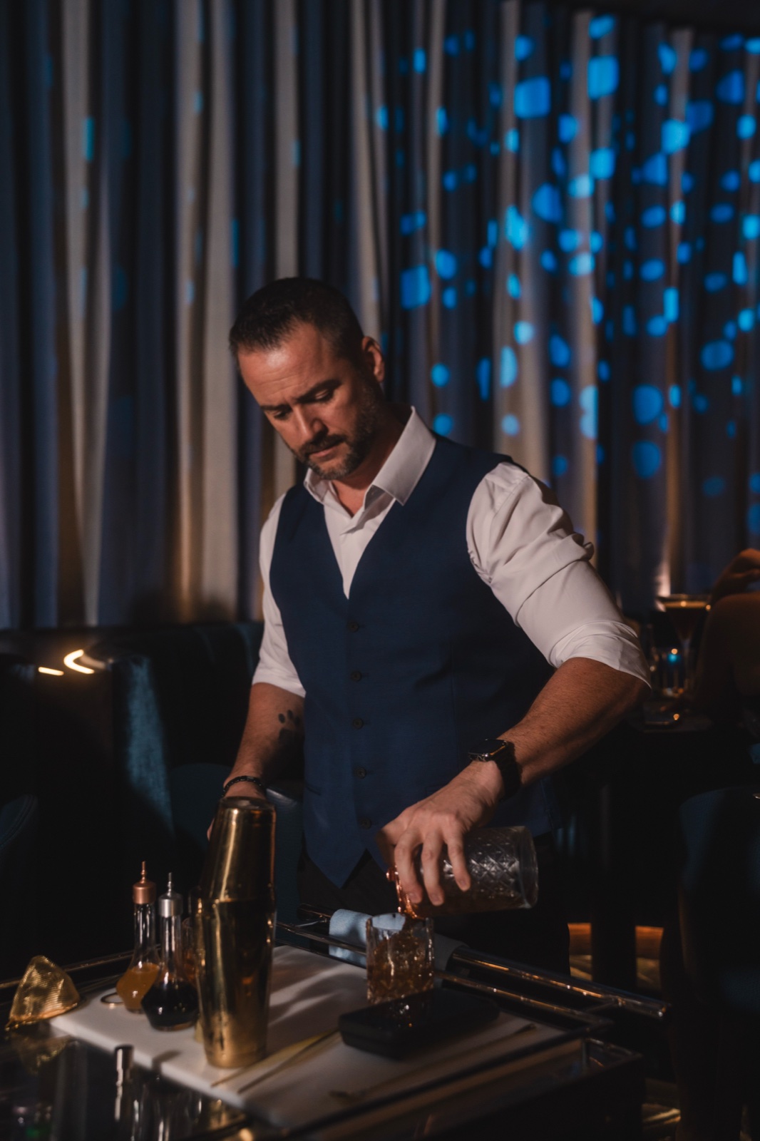 Bartender in a vest pouring a cocktail, focused