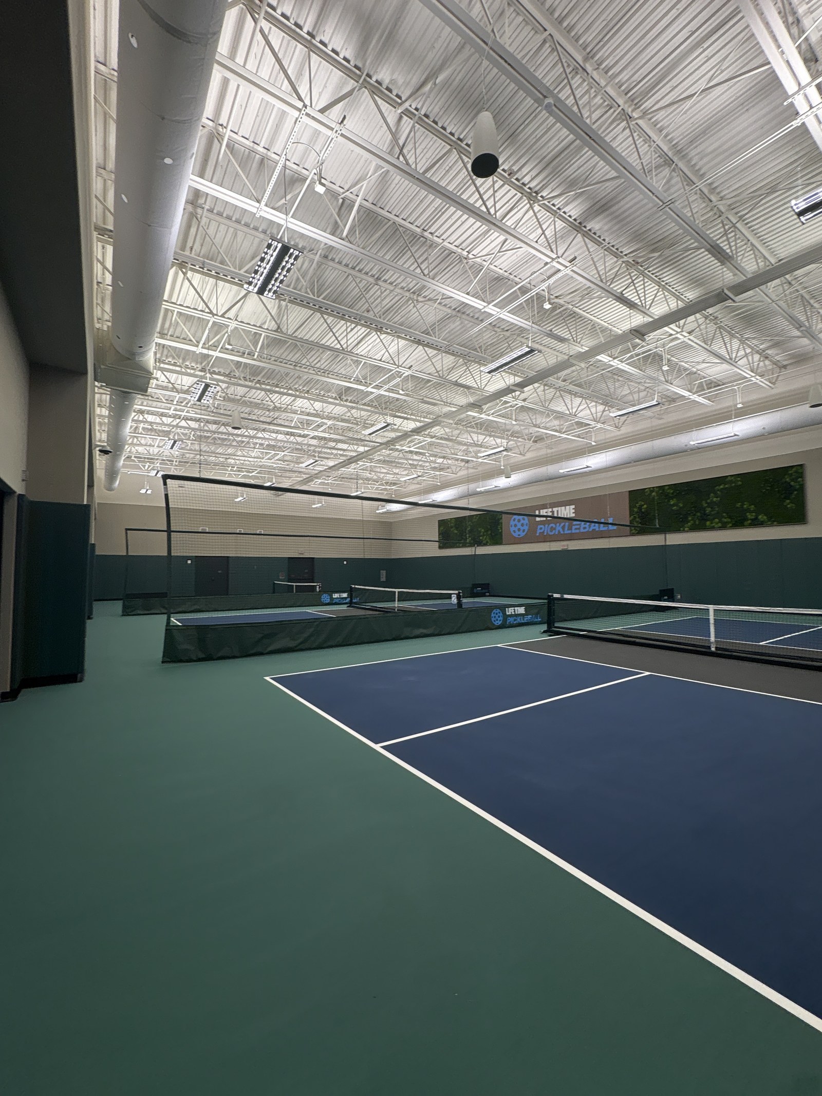 Indoor pickleball courts with blue and green surfaces under a high ceiling.