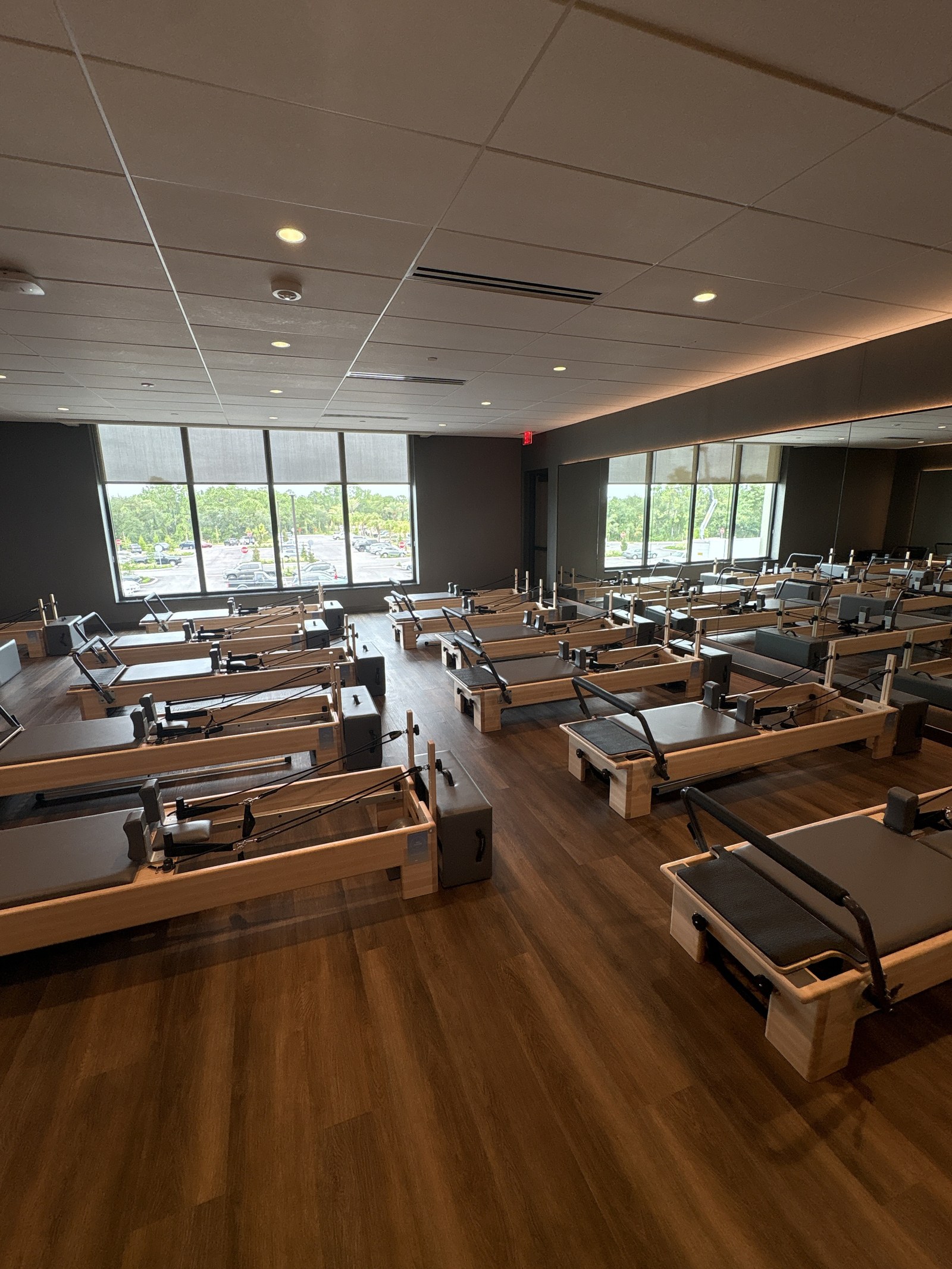 Reformer machines lined up on a wood floor beside large windows.