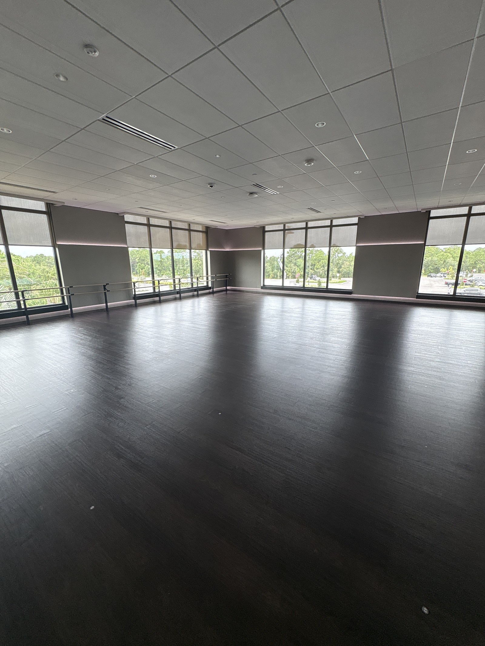 An empty group fitness studio with a dark wood floor and a wall of windows.