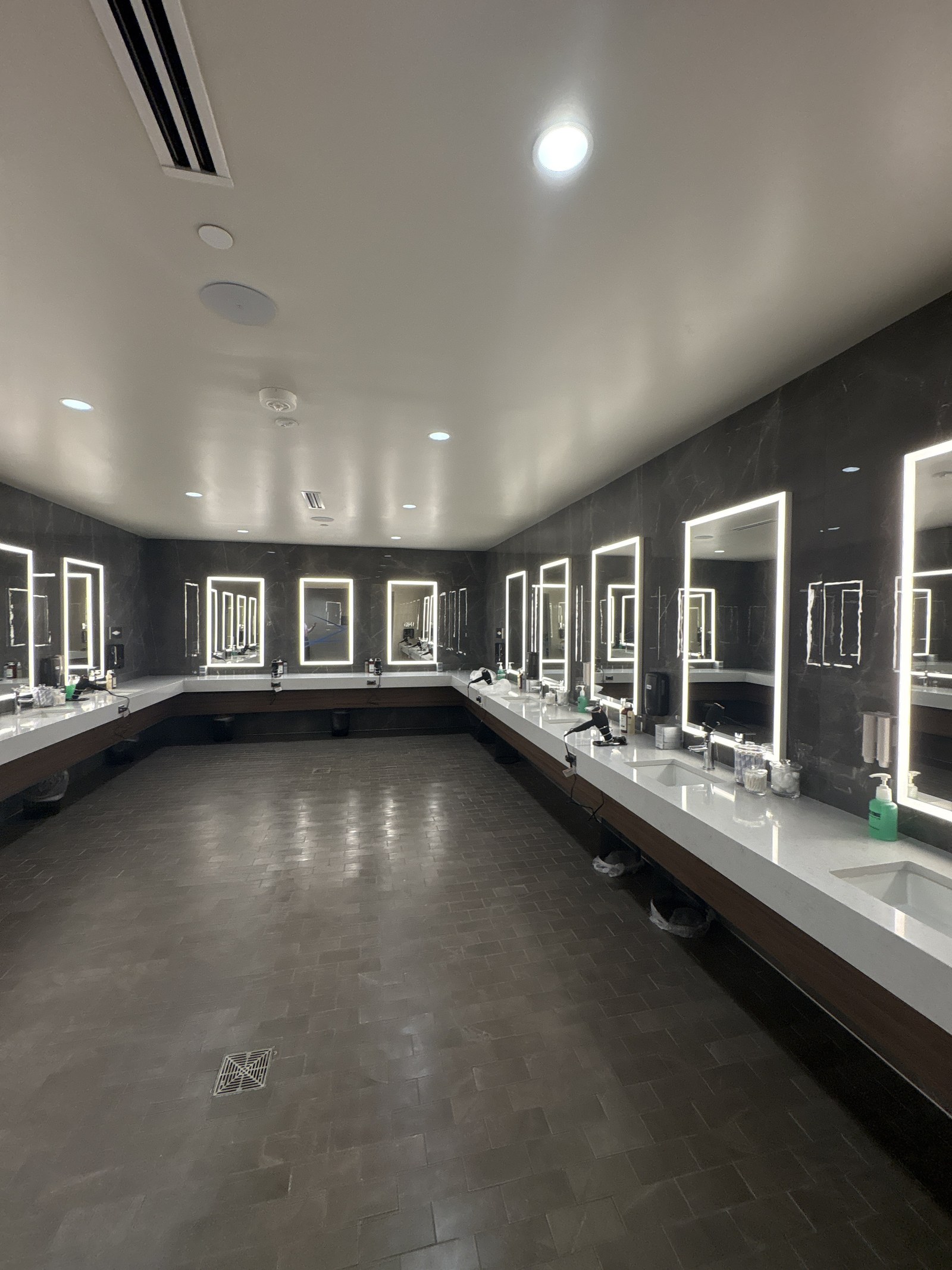 A long locker room vanity with lit mirrors and sinks.