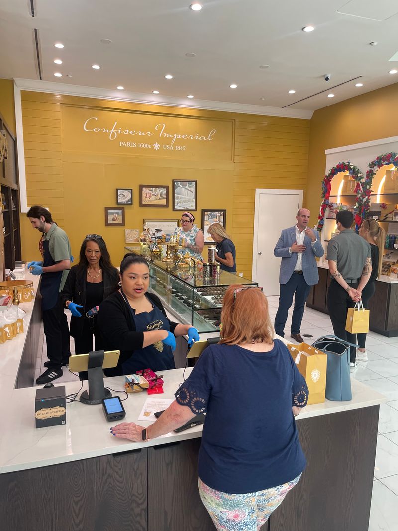 Customers at the counter inside the boutique, with the Confiseur Imperial lettering on the wall behind the display case.